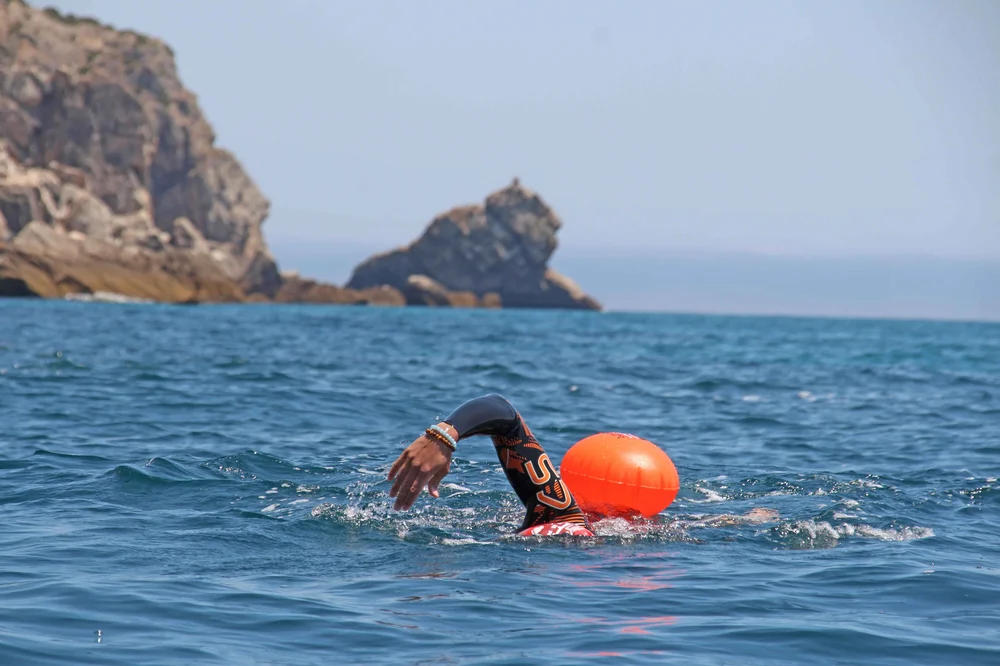 Sesimbra Abandoned Cape Tour Swimmer wearing an orca wetsuit and a SwimSecure buoy training on the coast of Sesimbra to cross the