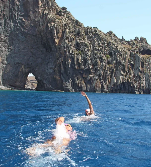 Two swimmers swimming together towards an impressive marine arch on the island of Madeira