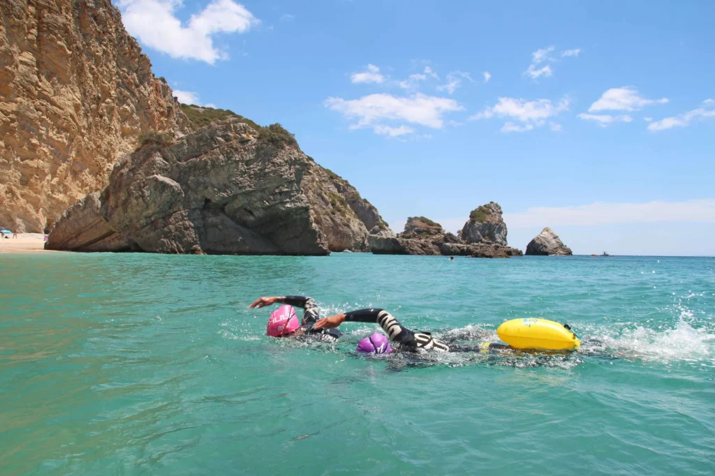 Two swimmers swimming together in the white endless sandy beach and crystal clear waters of Praia da