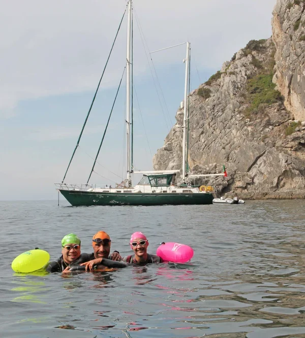 Three swimmers of different nationalities smiling in front of their yacht